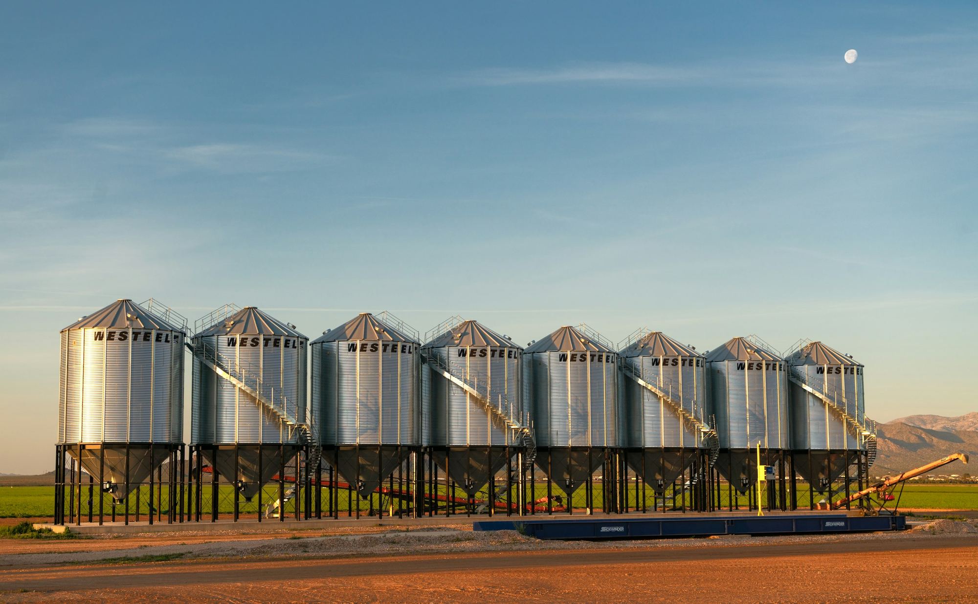 A row of steel grain silos at dusk